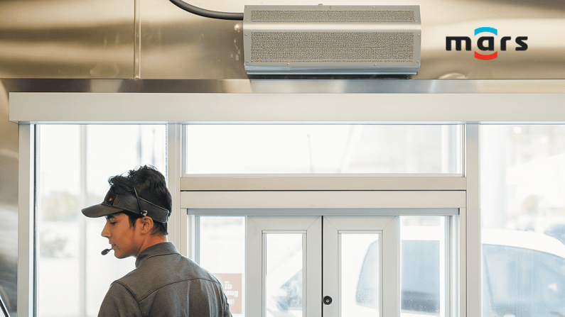 Man at take out window faces sideways. He's wearing a headset, grey shirt and visor. Above the take out window is an air system and next to that is the logo for Mars Air System.