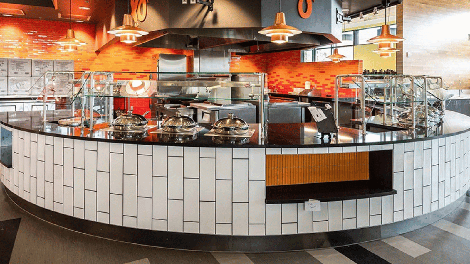 Curved serving counter with integrated glass food shields and stainless equipment in a modern open kitchen, designed for customer-facing foodservice operations.