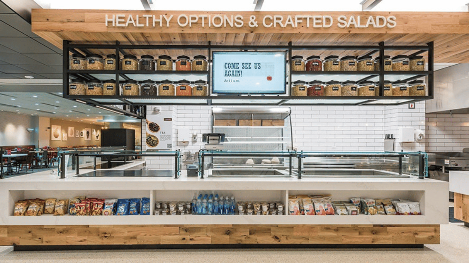 Contemporary serving line with low-profile glass food shields, wood accents, and grab-and-go display, supporting visibility and efficient customer flow.